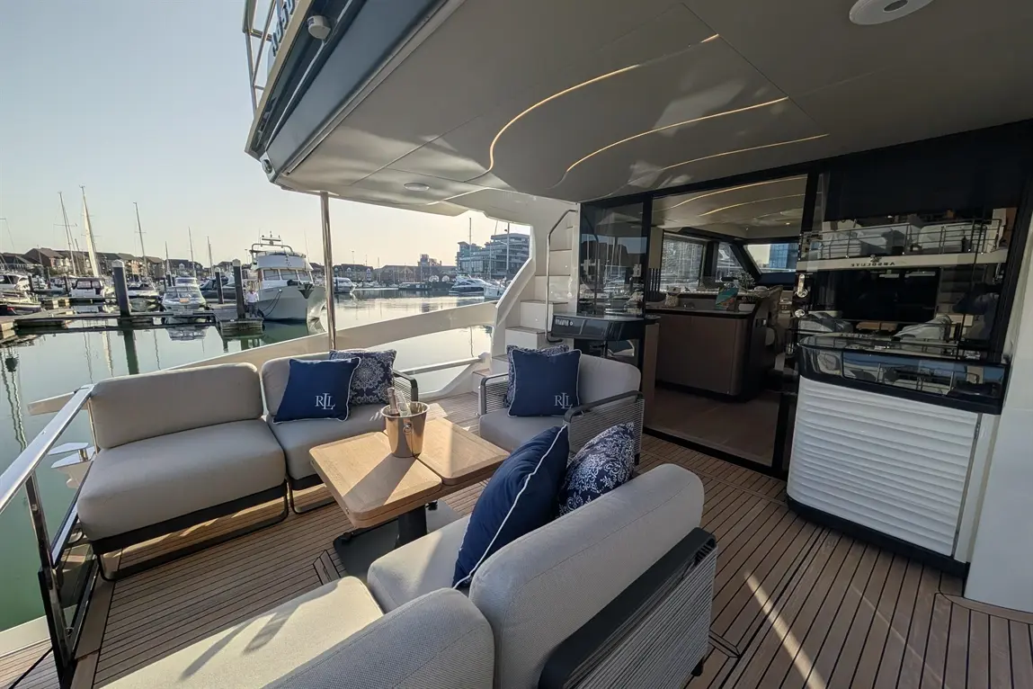 Luxury yacht outdoor seating area with plush furniture, a table, and harbour views. Visible text on cushions: "RJL".